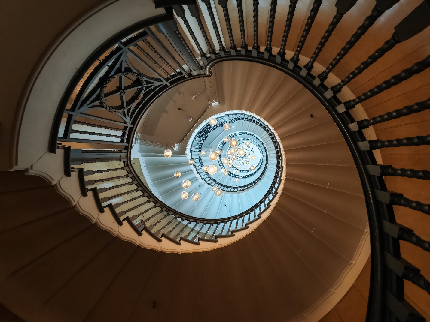 A spiral staircase with a chandelier

Description automatically generated